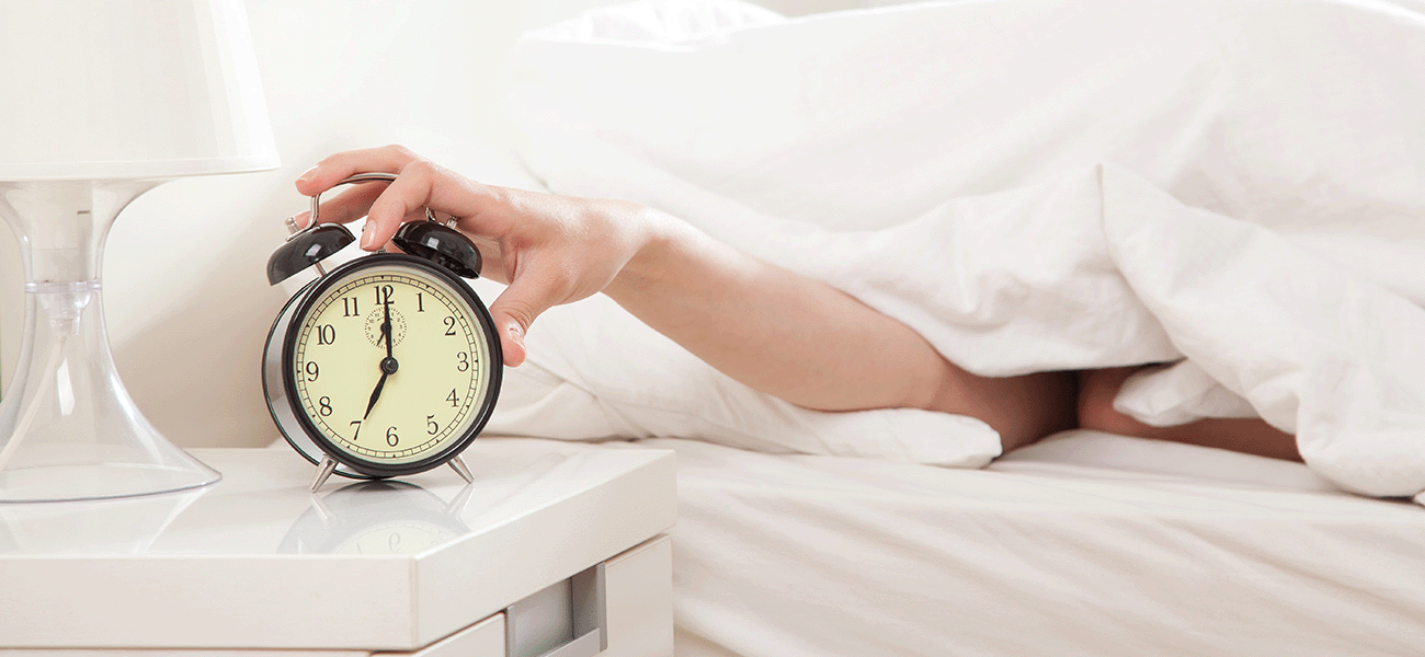 Hand reaching up from covers turning off alarm clock.