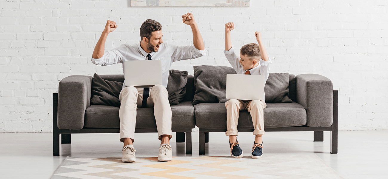 A happy father and son with laptops on their laps and hands in the air.
