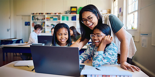 Image: A teacher assisting students on a laptop in class.